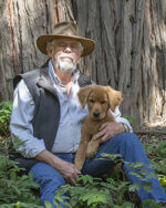 A man sitting in the woods holding a puppy.