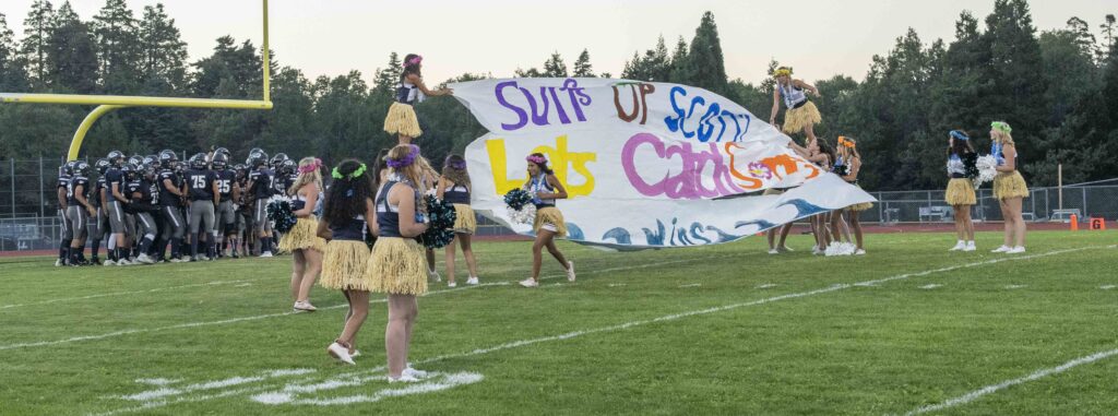 A group of cheerleaders holding a banner on a football field.