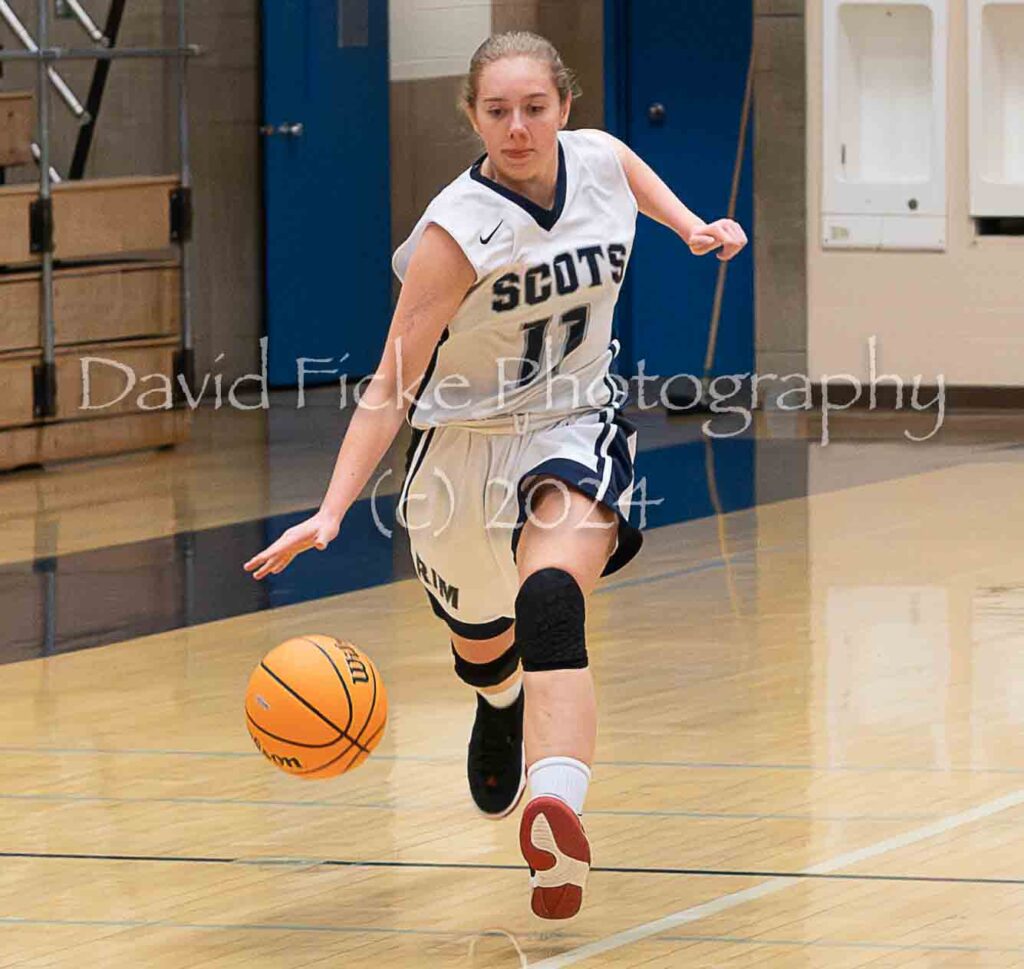 A female basketball player dribbling the ball on a court.