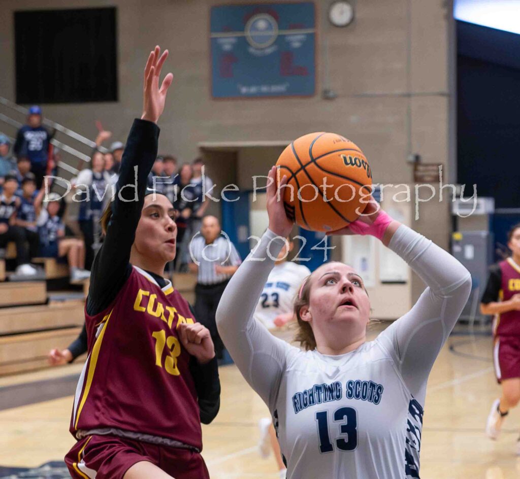 A female basketball player is trying to block a shot.