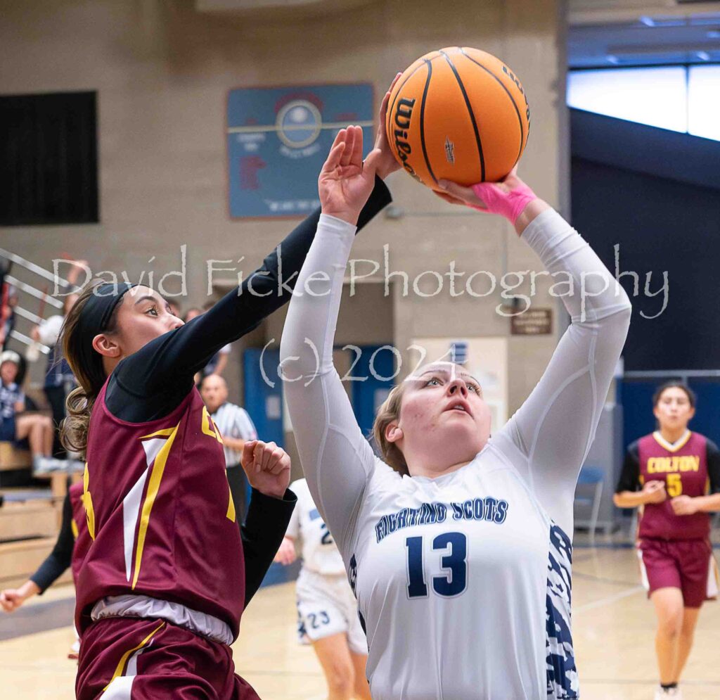 A girl is trying to block a basketball during a game.