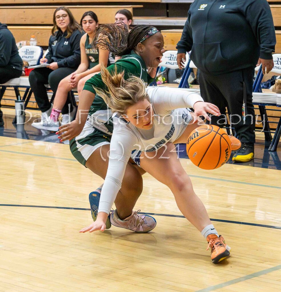 A female basketball player is trying to get the ball away from another player.