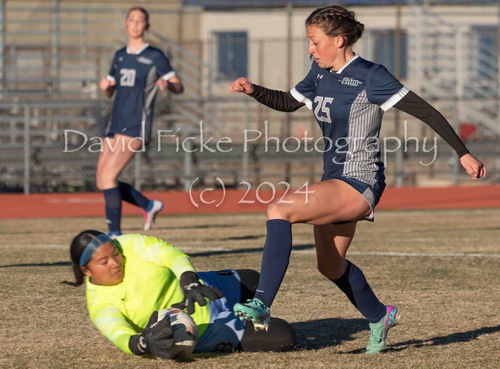A female soccer player tries to get the ball away from a goalkeeper.
