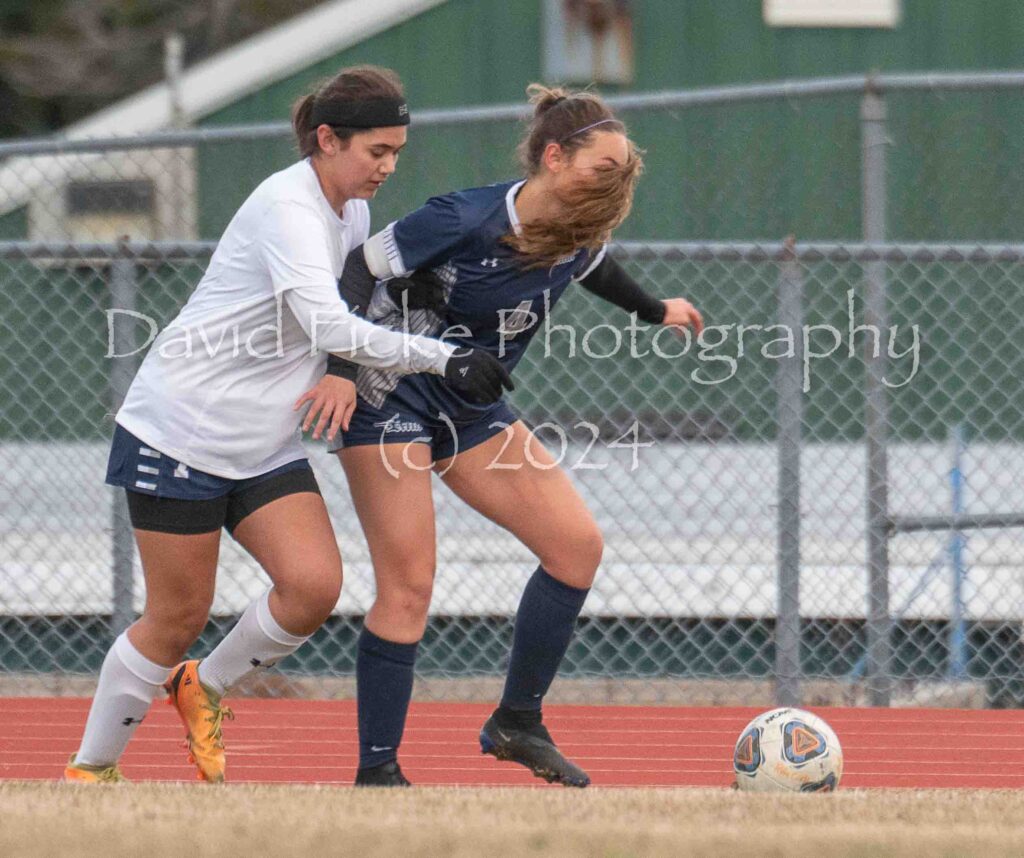 Two female soccer players fighting for the ball.
