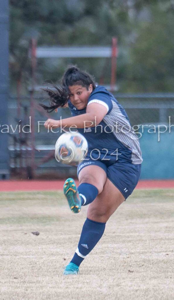 A female soccer player kicking a soccer ball.